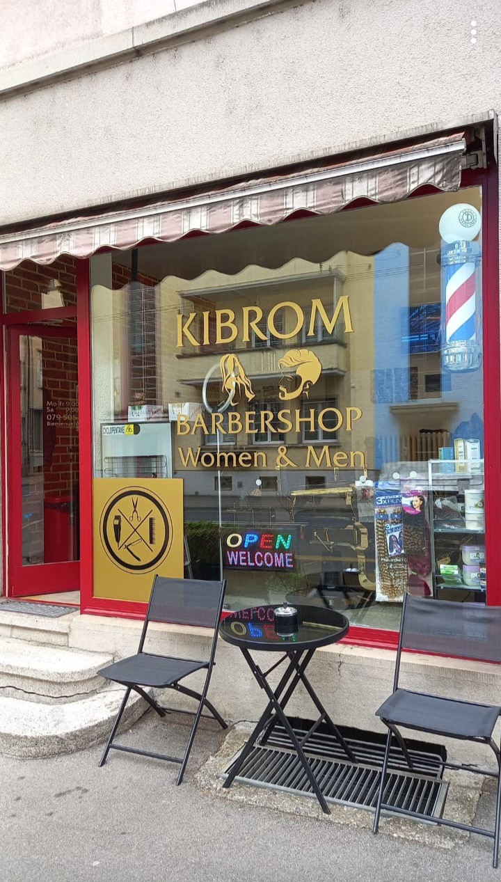 Ladenfront mit goldener Schrift «Kibrom Barbershop Women & Men», roter Rahmen und Barberstange